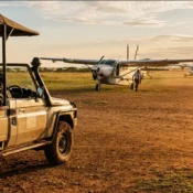 Aerial view of a safari aircraft landing on a dirt runway in the Masai Mara savanna.