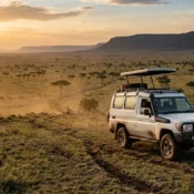 A 4x4 safari vehicle parked on a ridge overlooking the vast plains of the Masai Mara National Reserve.