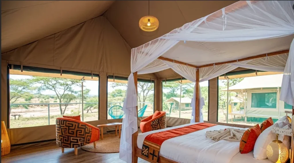 Interior of a luxury tent at Serenity Mara Legends Camp with a four-poster bed and large screen windows overlooking the river.
